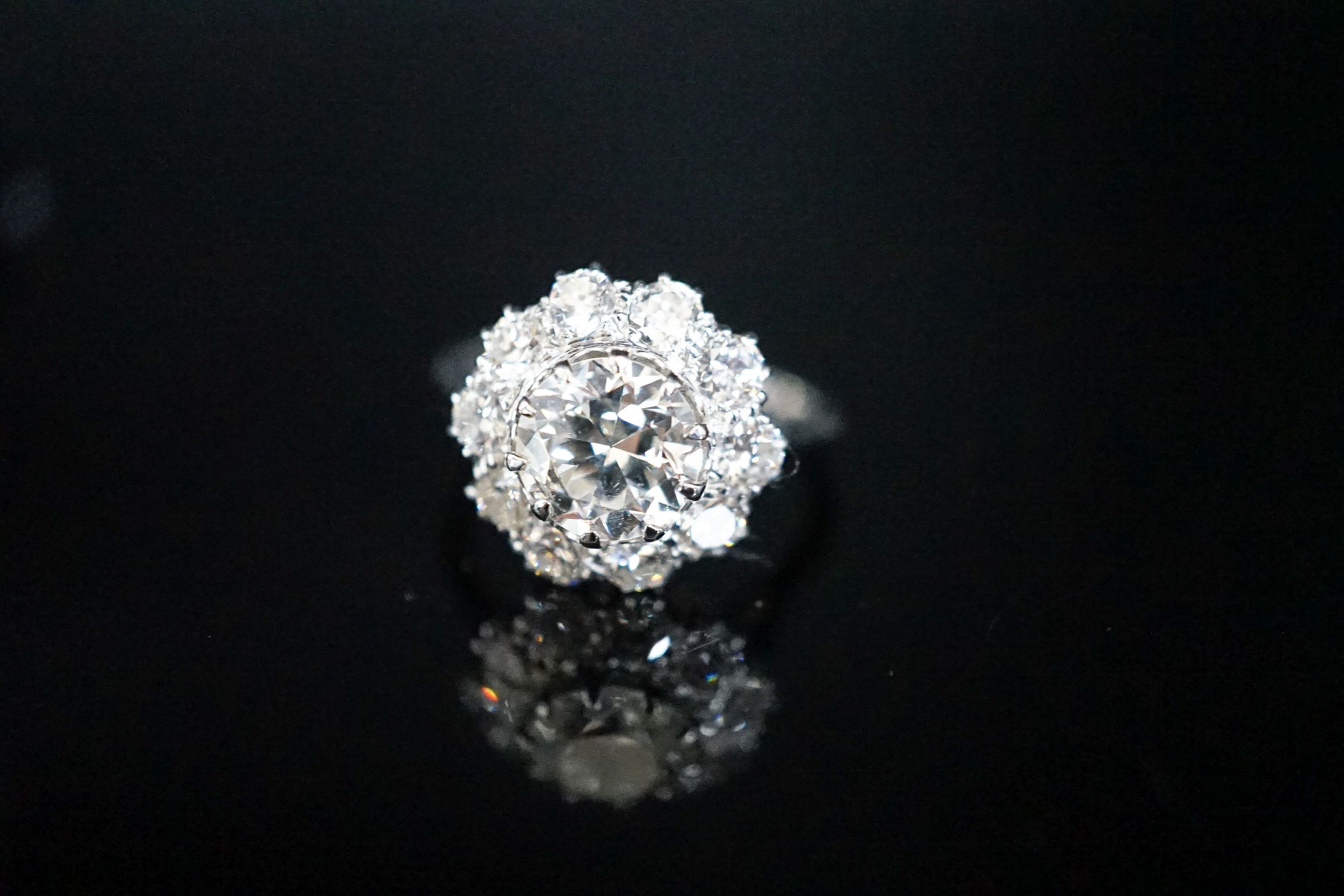 A white metal and eleven stone diamond set flower head cluster ring, the central stone weighing approximately 1.60ct, size N, gross 5 grams